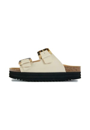 Cream slide sandal with two tortoiseshell buckles, cork footbed, and thick black ridged sole.