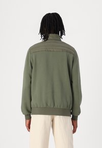 Sweatshirt vert olive avec un col montant, des poignets et un ourlet côtelés. Comprend un panneau arrière lisse et des épaules texturées. Design décontracté.