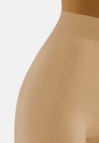 Leggings modellanti in nude con una texture liscia e leggermente lucida. Vita alta e design aderente, che si restringe verso la caviglia.