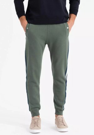Grønne joggingbukser med sidelængder, lavet af en blanding af bomuldsstof, elastiske manchetter, to frontlommer og minimalistisk design. Båret med beige sneakers.