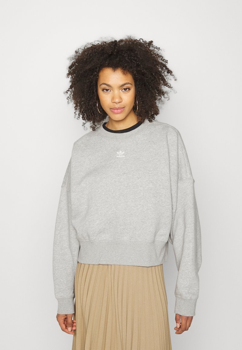 Felpa grigia corta con scollo rotondo, maniche lunghe e logo Adidas bianco sul petto. Caratterizzata da un tessuto morbido e con texture.