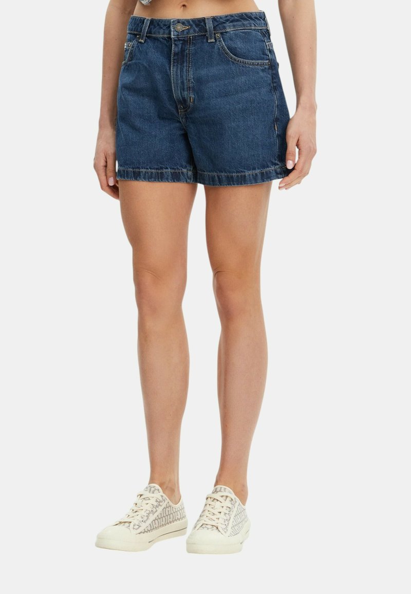 Shorts in denim blu scuro con un design a taglio dritto, caratterizzati da orli sfilacciati e tasche laterali, indossati con sneakers chiare.