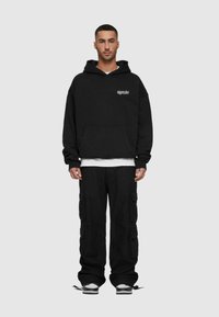 Black hooded sweatshirt with front pocket and embroidered logo, paired with loose-fitting black cargo pants featuring multiple pockets and drawstring cuffs.