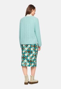Minzgrüner strukturierter Pullover, bunte gemusterte knielange Rock in Blau, Braun und Weiß, kombiniert mit beigen Ankle Boots mit Fellakzenten.