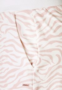Lichtroze en witte zebra gestreepte stof met een zachte textuur, met een witte elastische tailleband en een kleine gouden logo-tag.