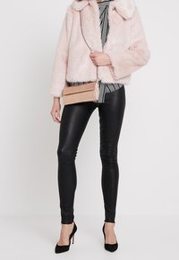 Rosa fuskpälsjacka med krage, över en randig topp; svarta läderleggings; liten beige axelremsväska; svarta klackar.