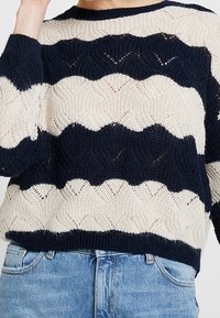 Strickpullover mit einem wellenförmigen Streifenmuster in Marineblau und Creme. Verfügt über einen runden Halsausschnitt, lange Ärmel und ein locker sitzendes Design.