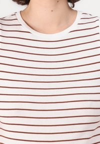 T-shirt en coton blanc avec des rayures horizontales marron, doté d'un col rond et d'une texture douce, idéal pour un look décontracté.
