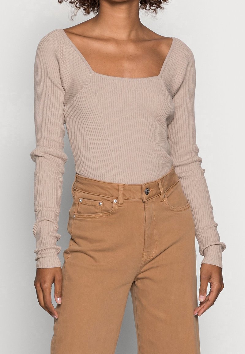 Maglia a maniche lunghe a coste di un beige chiaro con scollatura quadrata, abbinata a pantaloni marroni a vita alta con tasche e chiusura a bottone.