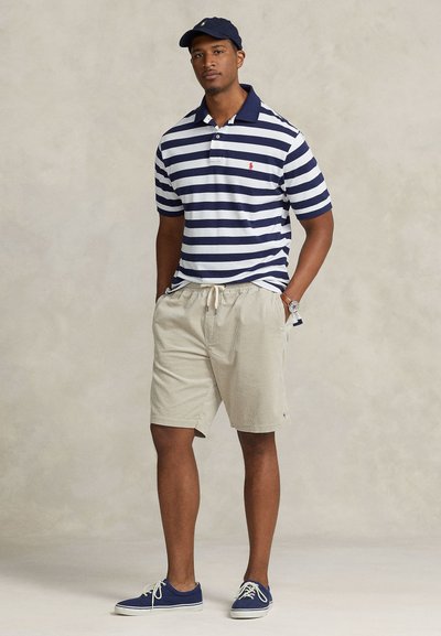Ριγέ μπλε ναυτικό polo με γιακά, μπεζ υφασμένα σορτς και μπλε αθλητικά παπούτσια. Συμπληρωμένο με μπλε καπέλο και ασημένιο ρολόι.