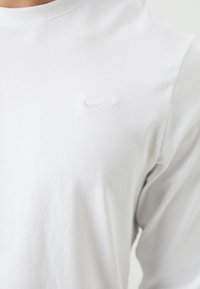 Baltas medvilnės ilgomis rankovėmis marškinėliai su subtiliu siuvinėtą Nike logotipu ant krūtinės. Lygus tekstūros ir apvalus iškirpimas.