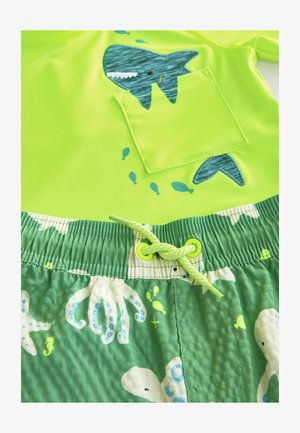 Top da bagno verde brillante con design a tasca a forma di squalo, abbinato a pantaloni corti verdi a fantasia con polpi e pesci, cintura elastica con lacci.