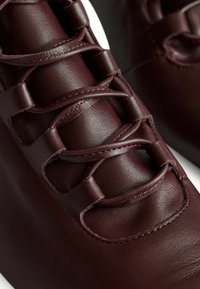 Zapatos de cuero burdeos con superficie texturizada y punta redonda. Presentan cordones con lazos y detalles de costura en contraste.