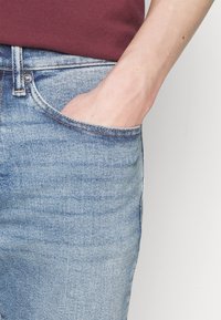 Ljusblå denimjeans med en framficka och en tajt passform, med ett blekt tvätt och kontrasterande sömnadsdetaljer.