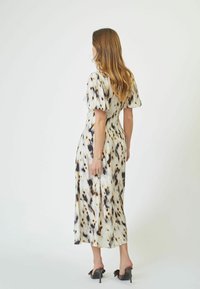 Long, flowy dress in light fabric featuring a beige, black, and brown spotted pattern, short puff sleeves, and a form-fitting silhouette.
