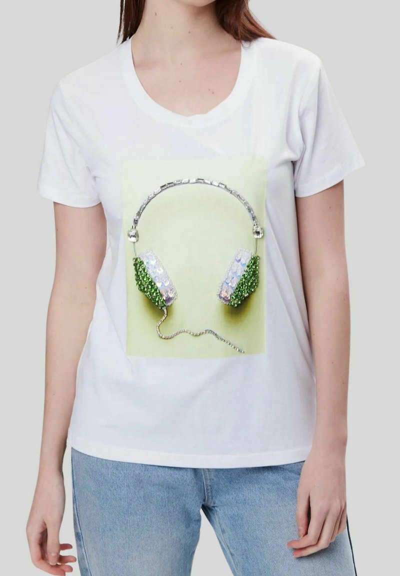 Camiseta blanca con un diseño gráfico de auriculares verdes y plateados con adornos similares a cristales en las almohadillas de las orejas y un cordón plateado.