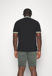 Black short-sleeve polo shirt with green and gray trim, paired with green shorts, featuring a rolled hem and back view.