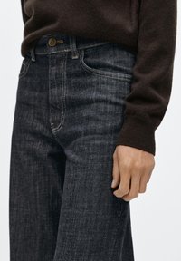 Mörkblå jeans i denim med figurnära midja, raka ben och diskret blekning. Gyllene sömmar framhäver fickorna och knappen.