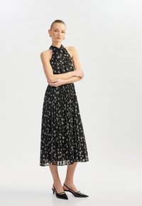 Svart blommig midi-klänning med halterneck, plisserad design och tunna axelband. Har små vita blommor utspridda över hela klänningen och en flödande siluett.