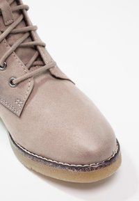 Světle hnědé semišové šněrovací boty s kulatou špičkou, kontrastním prošíváním a gumovou podešví s texturovaným povrchem.