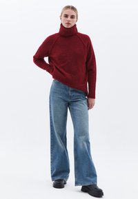 Rode gebreide trui met een hoge col, geribde manchetten en onderrand. Gecombineerd met lichtblauwe wijde jeans en zwarte stoere laarzen met een dikke zool.
