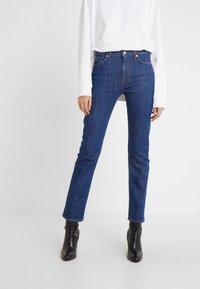 Hubené modré džíny z denimu s vysokým pasem a jemnými švy, spárované s volně střiženým bílým topem a kotníkovými boty.