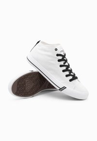 Sneakers alta in tela bianca, con lacci neri, un tallone nero e una suola in gomma marrone testurizzata con un motivo geometrico.