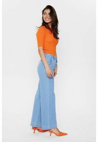 Ribota oranžā īsā piedurkņu blūze saskaņota ar gaiši ziliem platā stila džinsiem un oranžiem špiczābakiem. Gluda tekstūra, pieguļošs stils un ikdienišķs izskats.