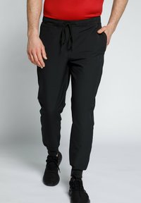 Schwarze Jogginghosen aus leichtem Material mit elastischem Bund und Kordelzug, schmal zulaufenden Beinen und gerippten Bündchen, kombiniert mit schwarzen Sneakers.