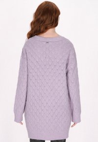 Maglione oversized di colore lilla con un motivo a rete a rombi, polsini a costine e scollatura rotonda. Texture morbida, vestibilità comoda e lunghezza fino a metà coscia.