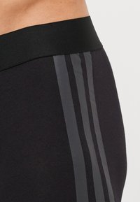 Calções de atletismo pretos com uma ampla cintura elástica e três riscas verticais cinzas de um lado, feitos de um tecido liso e elástico.