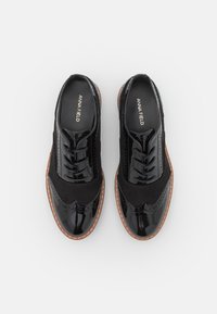 Ett par svarta oxfords-skor i patenterat läder och mocka med bruna sulor och snörningar, märkta "ANNA FIELD" på insidan, visade uppifrån mot en vit bakgrund.