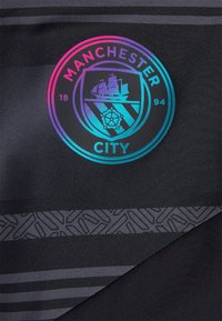 Black fabric featuring the Manchester City logo in iridescent colors, with patterned dark gray stripes and a textured accent along the edge.