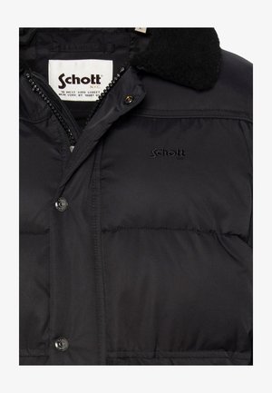 Zwarte pufferjack met ritssluiting, gewatteerde textuur en logodetails. Voorzien van een zachte, zwarte fleece kraag en knoopaccenten.