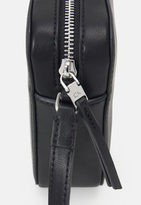 Borsa in pelle nera con cerniera argentata. Presenta una texture liscia, forma rettangolare e un dettaglio hardware con marchio.