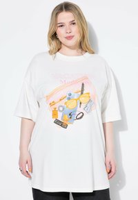 Hvid oversized t-shirt i bomuld med et farverigt ferietema grafisk design, der inkluderer solbriller, blomster og forskellige rejseartikler.