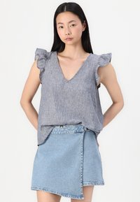 Grå linbluse med ruffleærmer, v-halsudskæring og en løs pasform, parret med en lys blå denim indpakningsnederdel.