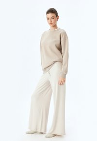 Sudadera beige con cuello redondo y corte relajado, acompañada de pantalones anchos a juego, confeccionados en una suave tela texturizada.