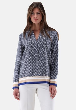 Marineblaue Bluse mit einem geometrischen Muster, ausgestattet mit V-Ausschnitt und langen Ärmeln. Am Saum befinden sich Akzente in Beige und Blau.