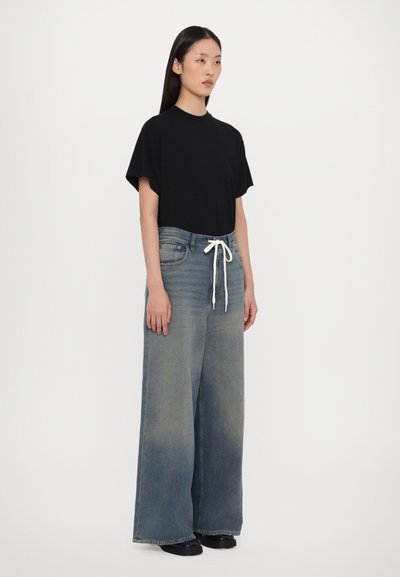 T-shirt nero a maniche corte abbinato a jeans in denim sbiadito a gamba larga con cordino bianco in vita. Tessuto morbido con una leggera texture.