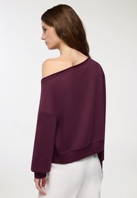 Felpa bordeaux a spalle scoperte con maniche lunghe, dal fit ampio e polsini a coste. Tessuto morbido con una texture liscia.
