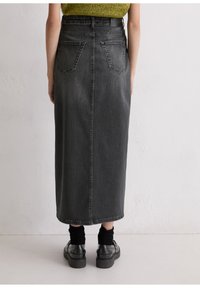 Zwarte denimrok met hoge taille en een rechte silhoutte, achterzakken en een zichtbare naad in het midden. Gepaard met zwarte schoenen en sokken.