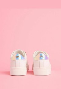 Zapatillas blancas con un acabado suave, que cuentan con acentos iridiscentes en el talón y un material texturizado. Suela plana, diseño minimalista.