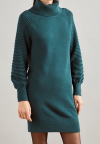 Robe-pull tricotée couleur sarcelle avec un col roulé haut et des manches bouffantes texturées. Poignets et ourlet côtelés. Corps lisse avec une coupe décontractée.