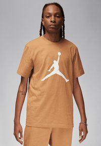 T-shirt in cotone marrone con un grande logo Jumpman bianco. Il collo rotondo e le maniche corte completano la sua vestibilità rilassata.