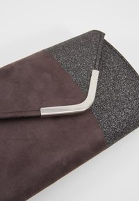Pochette en daim marron foncé avec des parties noires pailletées, avec un détail d’angle en métal argenté sur le rabat.