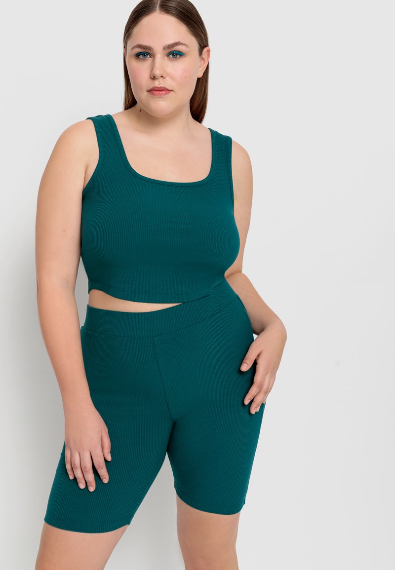 Top corto a coste teal con spalline larghe, abbinato a pantaloni corti a vita alta coordinati. Texture liscia, design aderente e senza chiusure visibili.