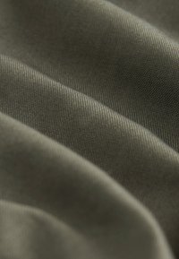 Tela de color caqui con una superficie lisa y texturizada, que presenta estrías diagonales y pliegues suaves que crean sombras sutiles.