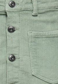 Tissu en velours côtelé vert clair avec des boutons-pression noirs et une poche carrée sur un vêtement.