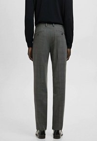 Pantalones a cuadros grises con un corte entallado, con dos bolsillos traseros y una textura de tela suave. Se llevan con zapatos negros y una blusa de manga larga.